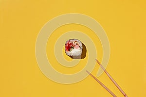 Fresh sushi roll and chopsticks on yellow background