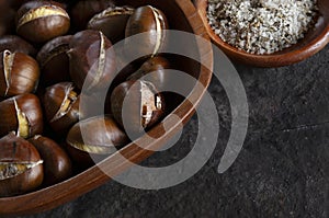 Fresh sweet baked edible chestnuts in wooden bowl with rosemary sea salt, closeup