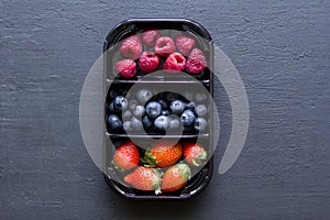Fresh Sweet Berries strawberries, blueberries and raspberries lie in the tray, box on Black Background. Harvest Concept. Mix