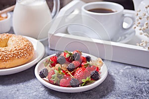 Fresh sweet berries on the white plate, bagel, cup of coffee and honey for breakfast.