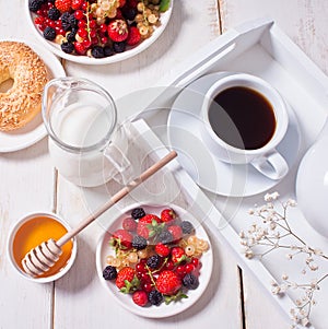 Fresh sweet berries on the white plate, bagel, cup of coffee and honey for breakfast