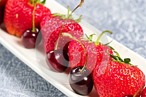 Fresh sweet cherries and strawberries on a white plate. healthy food, vitamins. on the grey table
