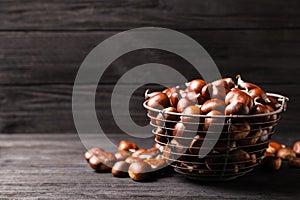Fresh sweet edible chestnuts in basket on black wooden table. Space for text