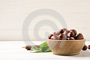 Fresh sweet edible chestnuts in bowl on white wooden table. Space for text