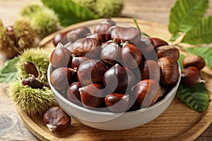 Fresh sweet edible chestnuts in bowl on wooden board