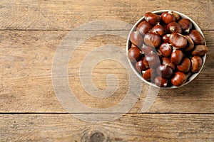 Fresh sweet edible chestnuts in bowl on wooden table, top view. Space for text