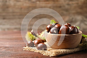 Fresh sweet edible chestnuts on brown wooden table, closeup. Space for text