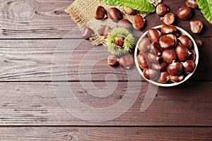 Fresh sweet edible chestnuts on brown wooden table, flat lay. Space for text