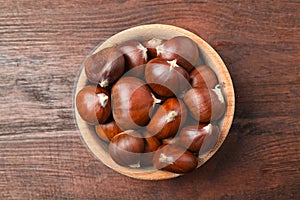 Fresh sweet edible chestnuts on brown wooden table, top view