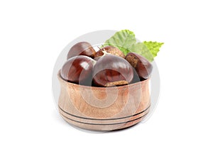 Fresh sweet edible chestnuts with leaves in wooden bowl on white background