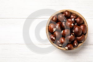 Fresh sweet edible chestnuts on white wooden table, top view. Space for text