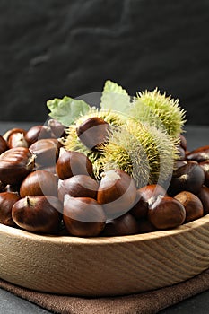 Fresh sweet edible chestnuts in wooden bowl on table, closeup