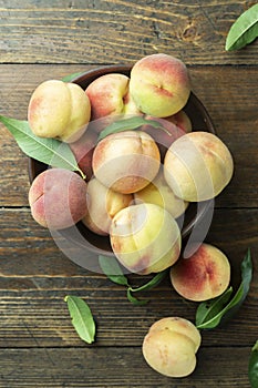 Fresh sweet peaches on the wooden table, selective focus. Fresh ripe peaches with leaves in a bowl