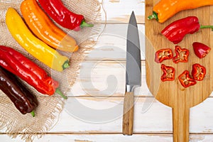 Fresh sweet pepper bell pepper on a cutting board with a knife. Chopped pepper pieces are ready to cook. Light wooden table, top