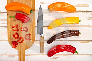 Fresh sweet pepper bell pepper on a cutting board with a knife. Chopped pepper pieces are ready to cook. Light wooden table, top