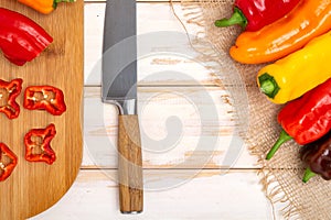 Fresh sweet pepper bell pepper on a cutting board with a knife. Chopped pepper pieces are ready to cook. Light wooden table, top