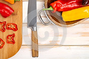 Fresh sweet pepper on a cutting board with a knife. Chopped pepper pieces are ready to cook. Light wooden table, top
