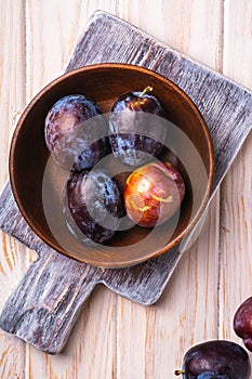 Fresh sweet plum fruits in brown wooden bowl on old cutting board, wood table background