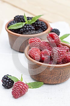 Fresh sweet red raspberry and blueberries in a clay pot and mint on light wooden table