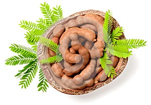Fresh tamarind fruits and leaves in the wooden bowl, isolated on the white background, top view