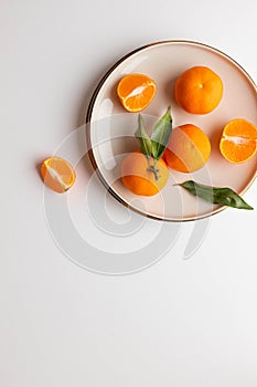 Fresh tangerine or clementin fruits on a beige plate with gold rim on a white background. Colorful fruit background. Flat lay, top