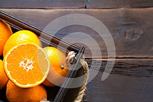 Fresh tangerines in brown box on wooden background with green fir branches. Frame, copy space, holiday and winter fragrance, new