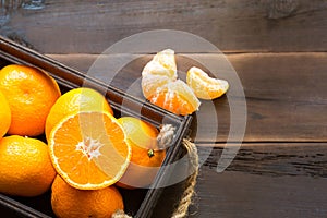 Fresh tangerines in brown box on wooden background with green fir branches. Frame, copy space, holiday and winter fragrance, new