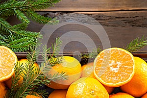 Fresh tangerines in brown box on wooden background with green fir branches. Frame, copy space, holiday and winter fragrance, new