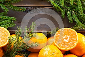 Fresh tangerines in brown box on wooden background with green fir branches. Frame, copy space, holiday and winter fragrance, new