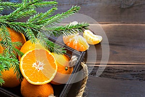 Fresh tangerines in brown box on wooden background with green fir branches. Frame, copy space, holiday and winter fragrance, new