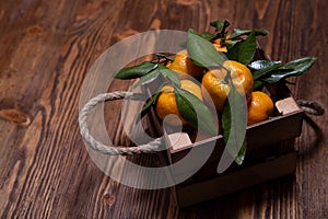 Fresh tangerines with leaves in an old box. On wooden background