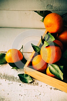 Fresh tangerines in an old box with leaves. On wooden background. Free space for text . Top view