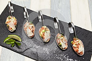 Fresh tartar Norwegian salmon on a small spoon on a black plate