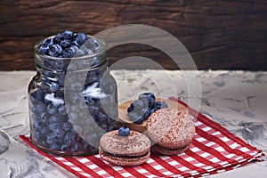 Fresh and tasty blueberry berries in a glass jar on a checkered napkin with sweet macaroons