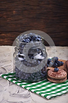 Fresh and tasty blueberry berries in a glass jar on a checkered napkin with sweet macaroons