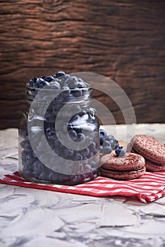Fresh and tasty blueberry berries in a glass jar on a checkered napkin with sweet macaroons