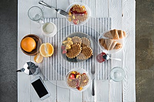 Fresh tasty breakfast with waffles, coffee and smartphone with blank screen on table