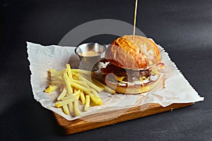 Fresh tasty burger on black background, served with sauce and french fries. Fast food, junk food concept.