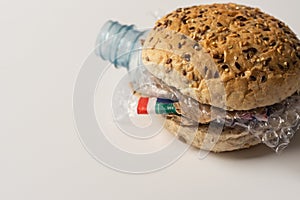 Fresh tasty burger with plastic waste and paper cardboard inside on white background. Recycled waste in our food concept