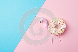 Fresh tasty donut in a shape of flamingo, on pink and blue background, top view