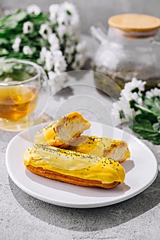 Fresh tasty eclair on white plate and cup of tea