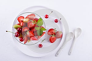 Fresh tasty mix fruit salad in the glass bowl on white table background. Healthy vitamin breakfast