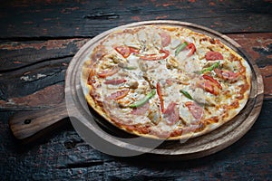 Fresh tasty pizza with chicken, tomato, paprika and mozzarella cheese on rustic wooden background