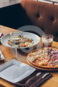 A fresh tasty pizza served with glass of white wine on the wooden table in the restaurant