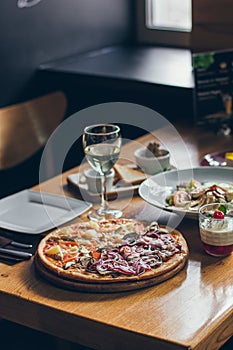 A fresh tasty pizza served with glass of white wine on the wooden table in the restaurant