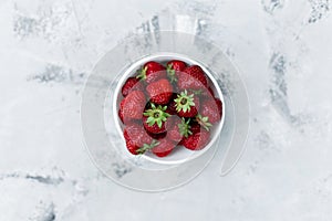 Fresh tasty strawberries in a white plate on a table with a white texture. Top view