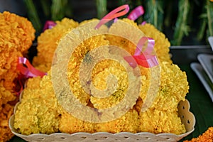 Fresh Thai style flower garlands made of bright yellow marigold with pink ribbon selling on basket in local market