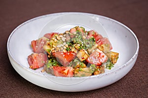 Fresh tomato and avocado salad with pine nuts and herbs on a white plate