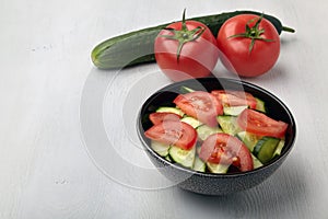 Fresh tomato and cucumber salad in dark bowl