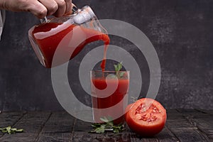Fresh tomato juice in a glass with tomatoes, with parsley on a dark background.